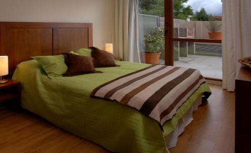 a bedroom with a green bed with a balcony at Bariloche Down Town Apartment in San Carlos de Bariloche