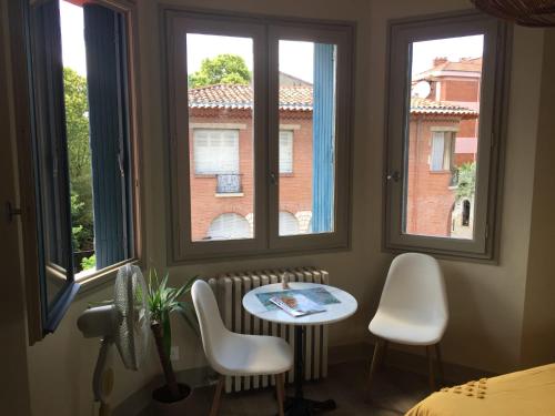 um quarto com uma mesa e duas cadeiras e janelas em CHAMBRE SPACIEUSE DANS MAISON ART DECO au CENTRE DE TOULOUSE em Toulouse