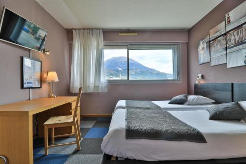 1 dormitorio con 2 camas, escritorio y ventana en Hôtel Les Flots Bleus en Savines