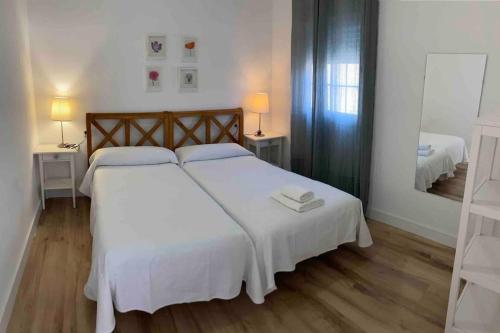 - une chambre avec un lit doté de draps blancs et d'un miroir dans l'établissement Moderno apartamento en San Bartolomé, à Séville