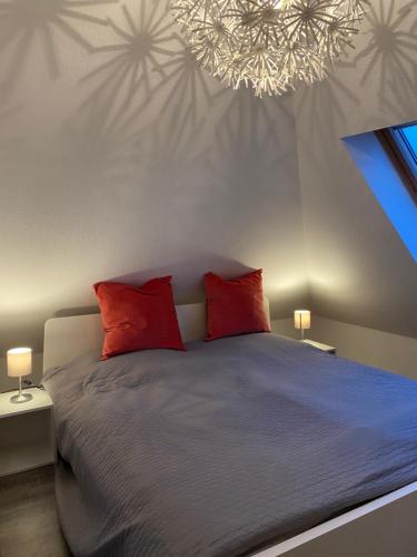 Un dormitorio con una cama con almohadas rojas y una lámpara de araña. en FeWo Herzstück - Neßmersiel, en Nessmersiel