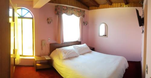 a bedroom with a white bed and two windows at Hotel Cordillera in Talca