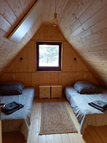 two beds in a wooden room with a window at Domek Pod Tylką in Grywałd