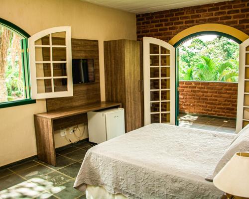 a bedroom with a bed and a tv and windows at Pousada Lago das Pedras in Juiz de Fora