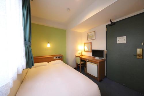 a bedroom with a bed and a desk with a computer at Smile Hotel Takaoka Ekimae in Takaoka