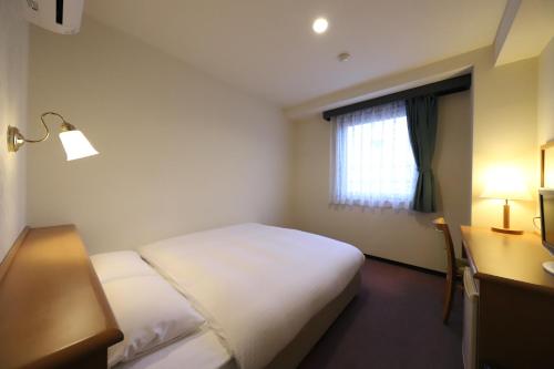 a hotel room with two beds and a desk and a window at Smile Hotel Takaoka Ekimae in Takaoka