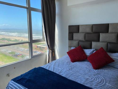 a bedroom with a bed with red pillows and a large window at Tenbury Beach Apartment in Durban