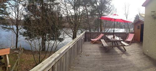 une terrasse en bois avec une table et un parasol rouge dans l'établissement Osez la Creuse - Au bord du lac de Vassivière - 27, à Royère-de-Vassivière