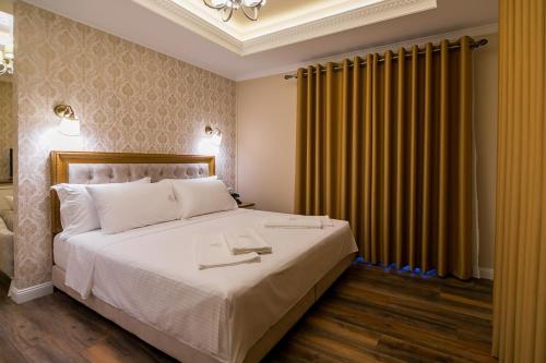 a bedroom with a large white bed and yellow curtains at Legacy Boutique Hotel in Korçë