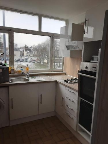 une cuisine avec des placards blancs et une grande fenêtre dans l'établissement Chez Lalis, Évry-Courcouronnes