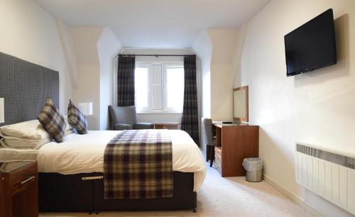 um quarto de hotel com uma cama e uma televisão em The Royal Hotel em Portree