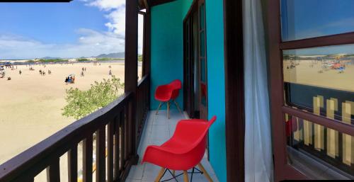 a balcony with two red chairs and a beach at Casa Rio - 04 Quartos de Frente para o Mar in Guarda do Embaú