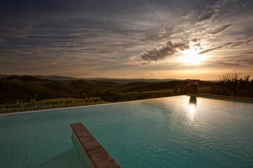 a large swimming pool with a sunset in the background at Fattoria Armena in Buonconvento
