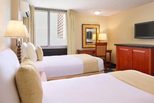 a hotel room with two beds and a television at Ewa Hotel Waikiki in Honolulu