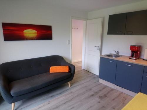 ein Wohnzimmer mit einem schwarzen Sofa und einer Küche in der Unterkunft Pension An der Reling in Dornumersiel