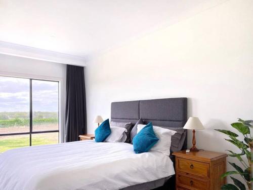 a white bedroom with a large bed with blue pillows at The Red Door @ Barossa Valley Vineyard View in Nuriootpa