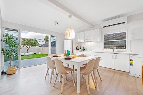 a white kitchen with a white table and chairs at 2 Min Walk to Beach Firepit Yard Kids welcome in Ettalong Beach