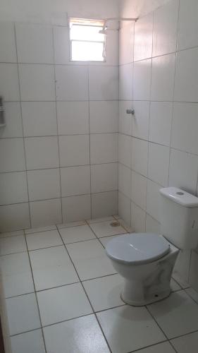 a white tiled bathroom with a toilet and a window at Casa em Itamaracá no Pilar, próximo da praia in Itamaracá