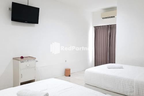 two beds in a white room with a tv on the wall at Roemah Proklamasi Syariah Mitra RedDoorz in Kampungdurian