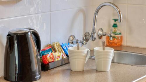 a kitchen counter with three white cups next to a sink at Court Street Motel in Parkes