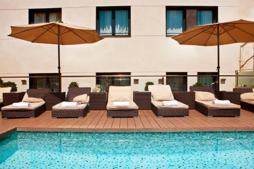 a pool with chairs and umbrellas next to a building at Grupotel Gran Via 678 in Barcelona