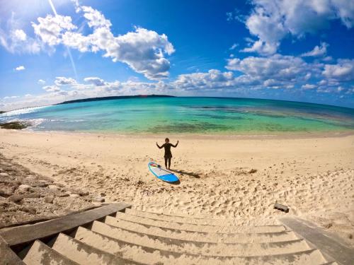 a person standing on a beach with a surfboard at Happy Island Miyako in Miyako Island