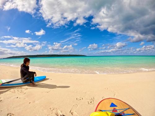 a person sitting on a surfboard on the beach at Happy Island Miyako in Miyako Island