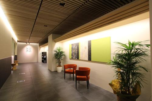 un couloir avec des chaises et des plantes dans un bâtiment dans l'établissement KOKO HOTEL Osaka Namba, à Osaka