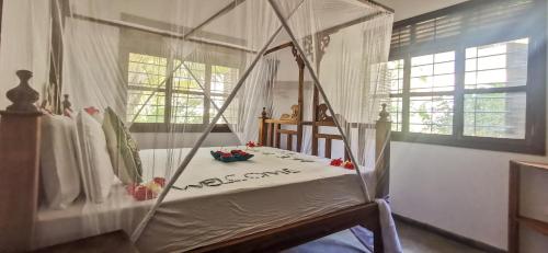 a bed with a canopy in a room with windows at Villa Malaika in Jambiani