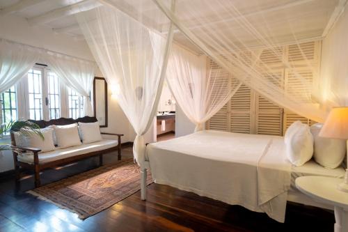 a bedroom with a white bed with curtains and a couch at Lion in the Sun Boutique Hotel & Spa in Malindi