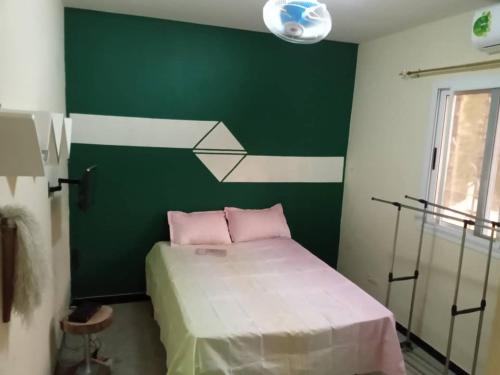 a bedroom with a green wall and a bed with pink pillows at Kër Adja in Ziguinchor