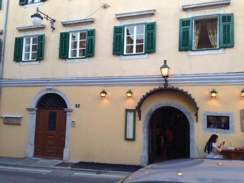 a woman sitting in front of a building with green shutters at Apartment Sand Beach in Opatija