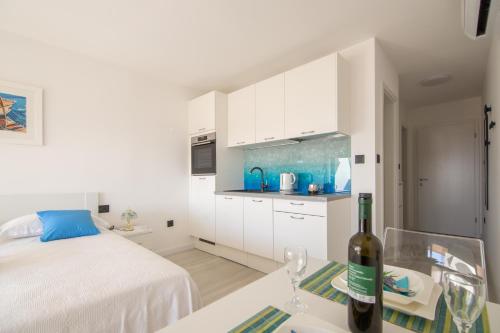 a white bedroom with a bed and a bottle of wine at Apartments Nona Draga in Komiža