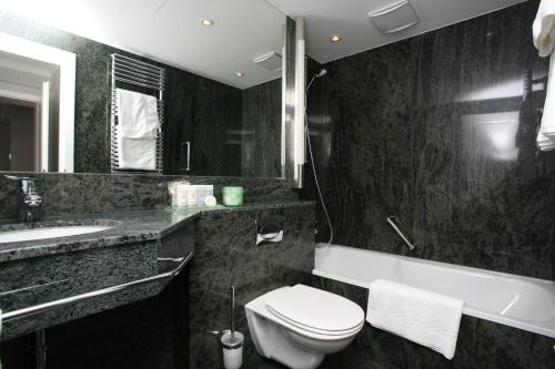 a bathroom with a toilet and a sink and a tub at AllgäuStern Hotel in Sonthofen