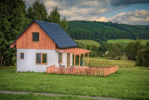 une petite maison avec un toit en gambrel dans un champ dans l'établissement Pastelova Krova - domki w Bieszczadach, à Ustrzyki Dolne