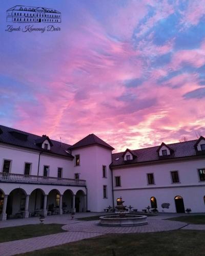 a sunset behind two white buildings with a pink at Zámek Kamenný Dvůr in Kynšperk nad Ohří