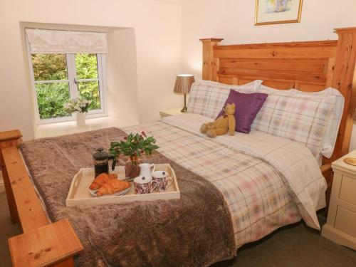 - un ours en peluche assis sur un lit avec un plateau de nourriture dans l'établissement Hope Cottage, à Castleton