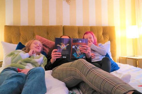 three girls laying on a bed reading books at Vänerport Lakefront Hotell in Mariestad