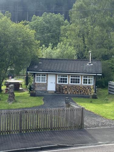 a small house with a fence in front of it at Pine Cabin, Strathyre. A cosy escape from it all. in Strathyre