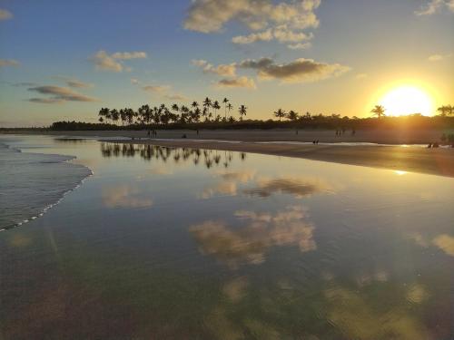 a sunset on a beach with palm trees and the water at Acalanto do Sargi in Uruçuca