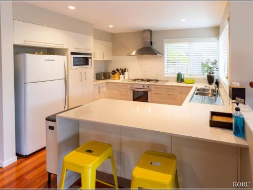 a kitchen with a white refrigerator and two yellow stools at Koru at Hyams Beach in Hyams Beach