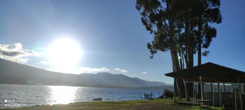 a lake with a house and a tree and the sun at HOSPEDAJE DON PABLO in Otavalo