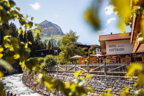 a building with a mountain in the background with yellow flowers at Hotel Gotthard in Lech am Arlberg
