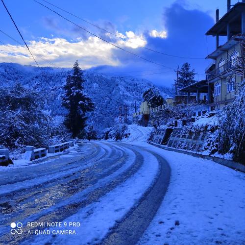 a snow covered road with a house in the distance at Trushali Homestay in Nārkanda