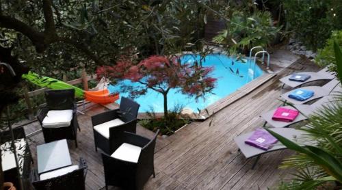 a pool with tables and chairs next to a wooden deck at Chambres d'hôtes des Oliviers in Coaraze