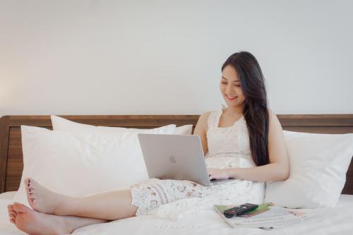 a woman sitting on a bed with a laptop at Play Poshtel & Cafe' in Krabi town