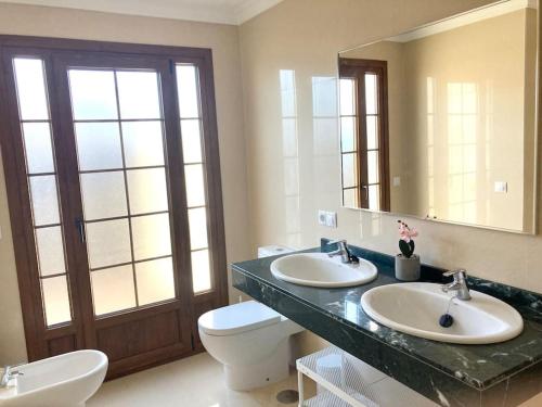 Un baño con dos lavabos, un inodoro y un espejo. en Luxury 4-Bedroom Villa With Heated Pool + Sea View, en Playa Blanca