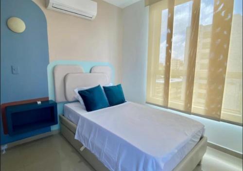 a bedroom with a bed with blue pillows and a window at Apartamento en Sector Ciudad Jardin Barranquilla cerca al Centro Comercial Unico in Barranquilla