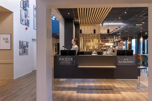 um lobby de um restaurante com uma mulher sentada num balcão em PADJA Hôtel & Spa Vannes em Vannes