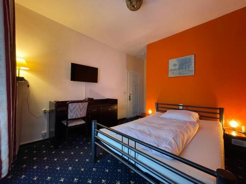 1 dormitorio con pared de color naranja, cama y escritorio en Hotel Kull von Schmidsfelden, en Bad Herrenalb